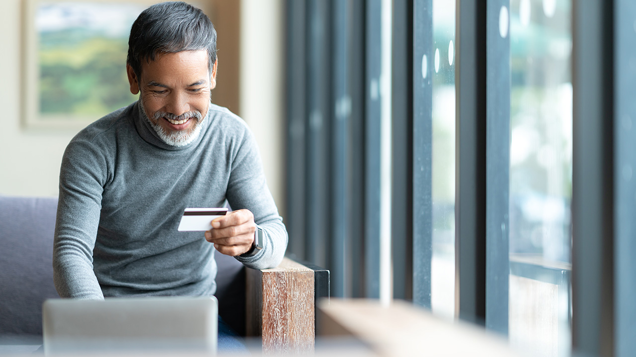 a man holds a credit card while using a laptop