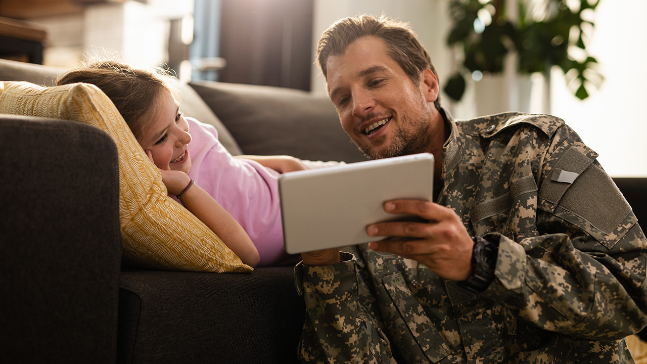 a military father looks at a tablet with his daughter