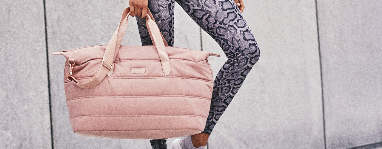 girl in athletic gear holding a FLY Weekender Bag in Blush Pink