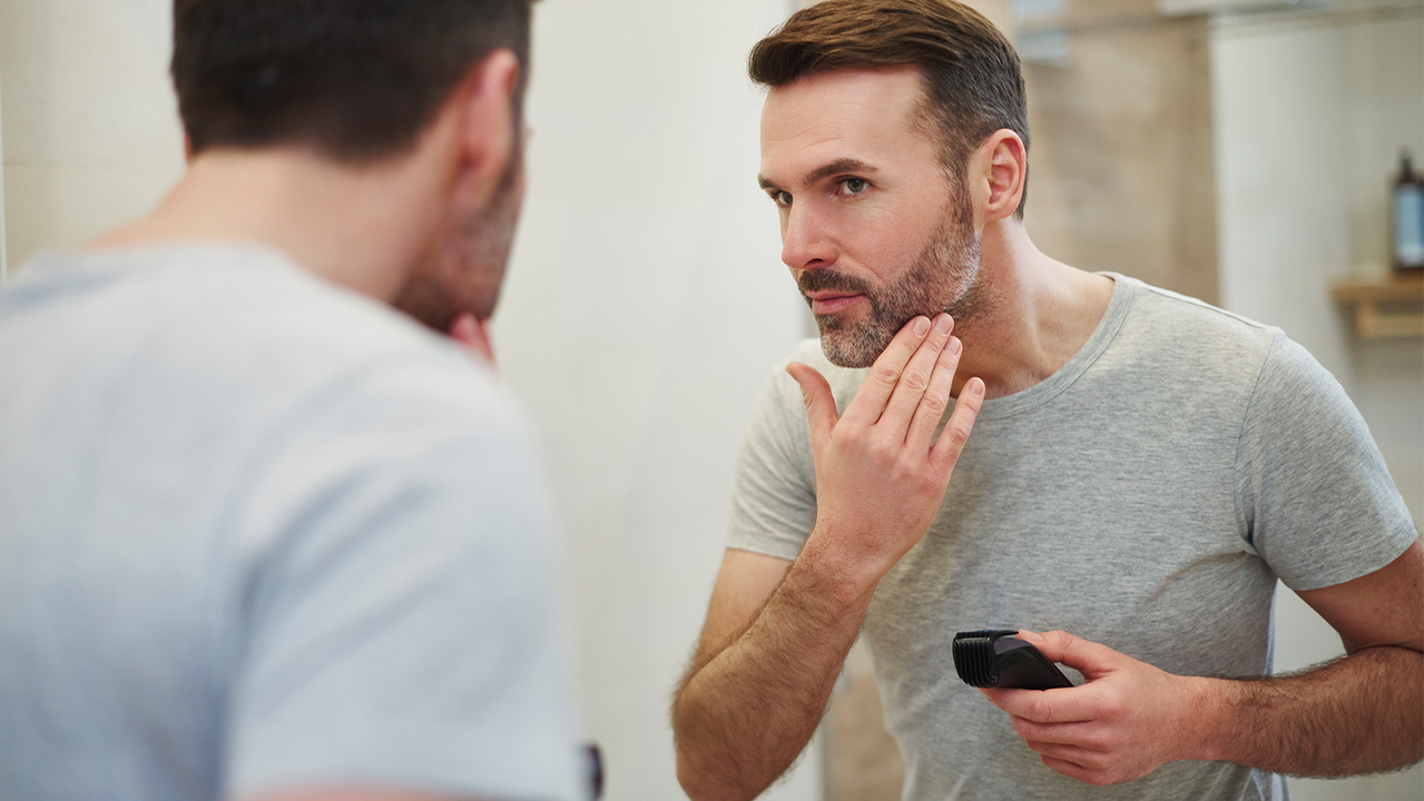 man shaving with electric razor reflection in mirror