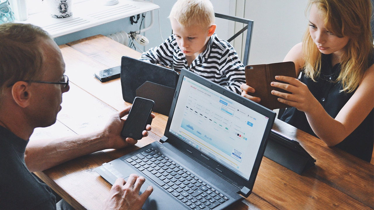 family sitting at table on electronic devices