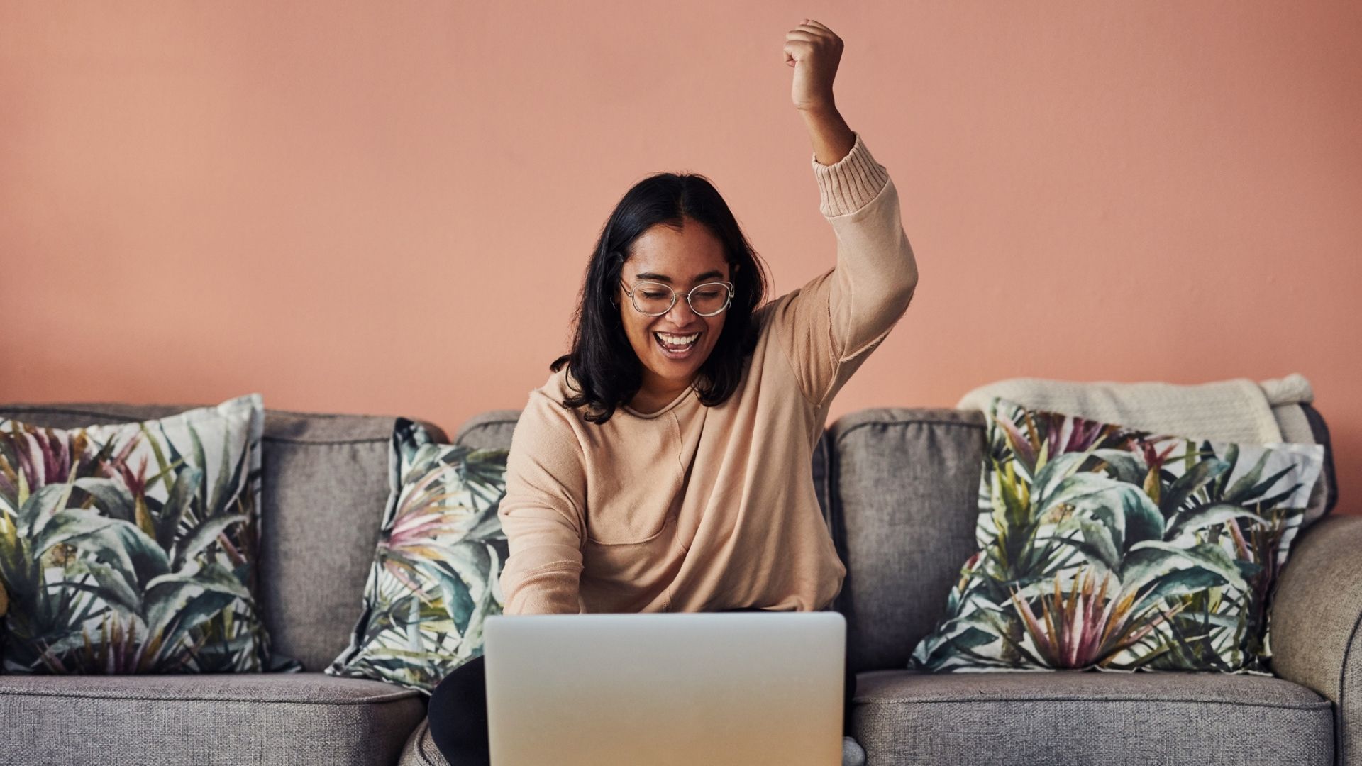 young woman cheering while using a laptop on the sofa at home