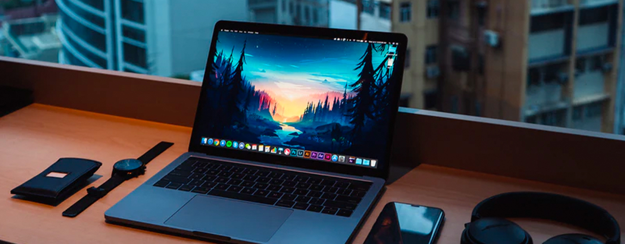 laptop macbook watch headphones and phone on table with city in background
