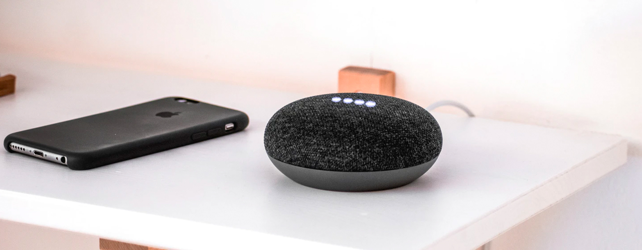 google home mini sitting on white shelf next to iphone