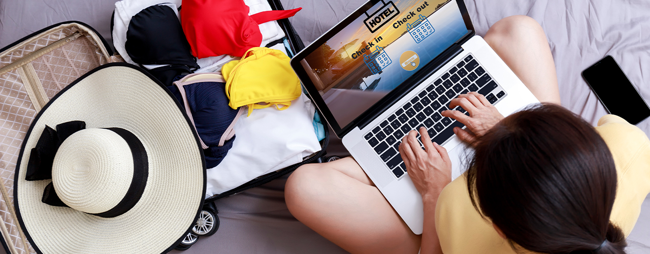 Top view Asian happy woman plan for trip by laptop booking hotel on the bed at home