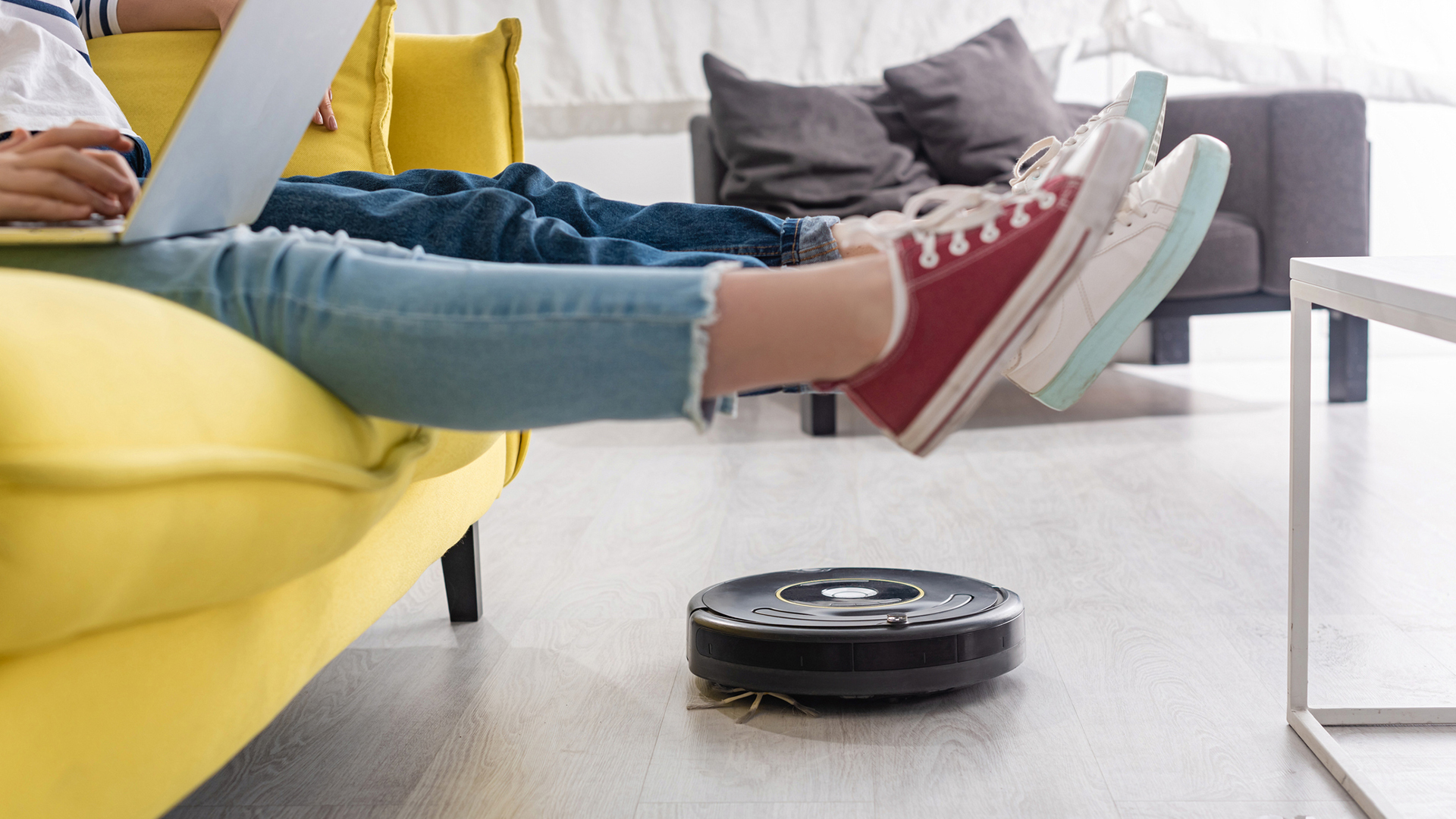 person on yellow couch lifting feet for robot vacuum